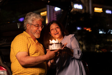 Happy Senior Citizen couple cutting birthday cake at night in the city