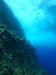 Underwater seascape, rocks and water surface with waves. Ocean ecosystem with stone wall and marine life. Underwater photography, scuba diving adventure.