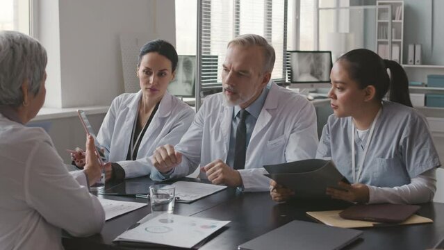 Waist up of group of multiracial medical colleagues having discussion at table during morning briefing in meeting roomWaist up of group of multiracial medical colleagues having discussion at table dur