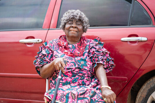 image african aged woman with grey hair sitting besides a car- portrait of black mother seated with a walking stick