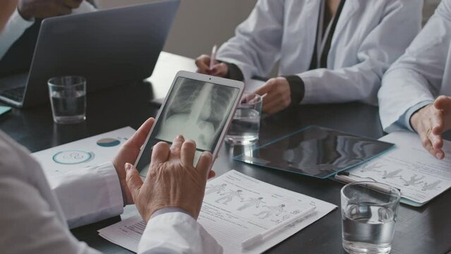 Cropped shot of unrecognizable female doctor wearing white lab coat using digital tablet while examining chest x-ray of patient during conference meeting with colleagues