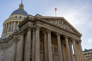 Fototapeta premium Pantheon building in Paris, France with focus on French flag over blue sky.