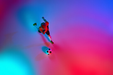 Obraz premium Aerial view of playing little boy during training with football ball in gradient red-blue neon light. Concept of action, sportive lifestyle, team game, health, energy