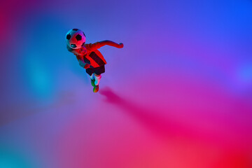 Top view of playing little boy during training with football ball in gradient red-blue neon light. Concept of action, sportive lifestyle, team game, health, energy