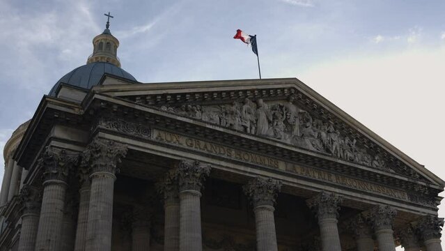 Pantheon building in Paris, France with focus on French flag over blue sky.