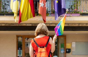 One woman standing alone in front of a government building holding a rainbow flag. Fight for rights concept