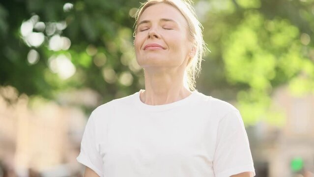Portrait of confident mature blond woman looking ahead and exhaling fresh air taking deep breath and reducing stress after work at park Successful businesswoman resting for peaceful mind outdoors