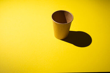 Cardboard coffee cup on yellow background with shadow.