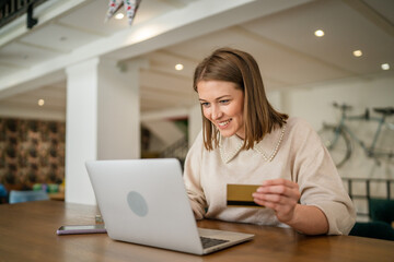 One young business woman holding credit card and shopping online on laptop, modern consumer concept