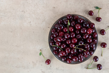 Bowl of fresh red cherries on beige background. Top view Copy space.