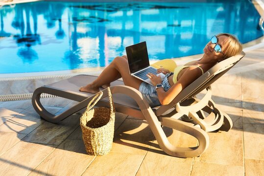 Hipster woman using laptop by the pool. Young girl freelancer working on a laptop while on vacation near the pool. High quality photo