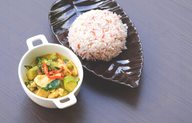 Chicken green curry with steamed rice in ceramic dish on wooden table top 