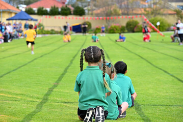 back of girl with team mates looking  down track at relay running race 