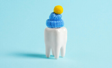 Fototapeta na wymiar Human tooth wearing little cute knitted hat on blue background. Winter advertisment for dental clinic.