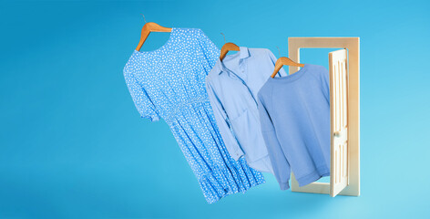 Clothes on hangers fly out of the open wooden door blue background. Shopping and sale concept advertising poster.