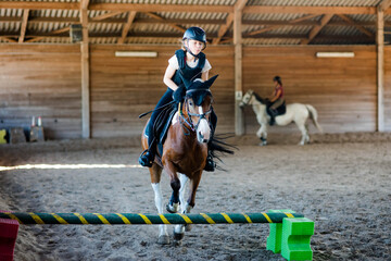 Pretty young girl doing equestrian show jumping on her pony in a farm - 617787564