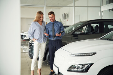 Fototapeta na wymiar Choosing the automobile. Man in formal clothes is with woman customer with the electric car