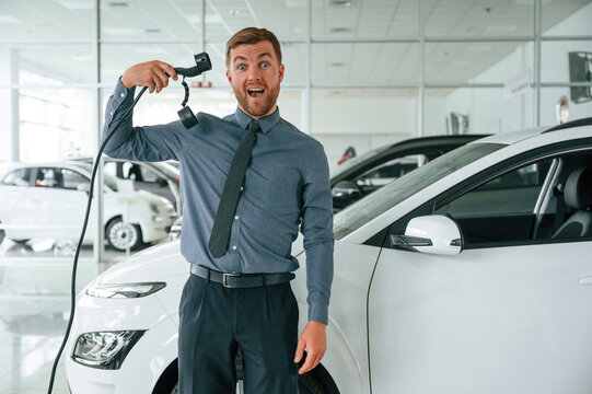 Having fun with charger. Handsome car dealership worker is with electric vehicle