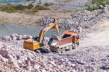 Excavator Pours Rock into a Heavy Dump Truck in a Stone Quarry