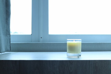 the burning luxury aromatic scented candle glass decorated on the wooden table to make better ambient scent on valentine day with background of sunlight from the window in morning