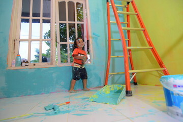 Fototapeta na wymiar CHILDREN HELPING THEIR PARENTS WORK PLAYING WALL PAINTING USING THE SIMPLE EQUIPMENT OF A LADDER AND A PAINT ROLLER
