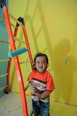 CHILDREN HELPING THEIR PARENTS WORK PLAYING WALL PAINTING
USING THE SIMPLE EQUIPMENT OF A LADDER AND A PAINT ROLLER