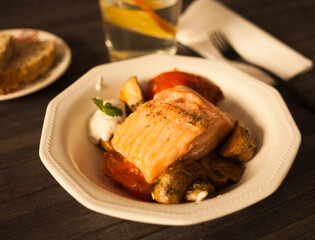 steamed sea trout fillet served on fried mushrooms with tomatoes in a white bowl