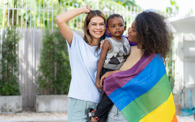 Lesbian couple playing rainbow flag with little child. Multiethnic woman and family happy leisure together outdoor. Diversity gay women, homosexual, LGBT, same gender mariage motherhood lifestyle.