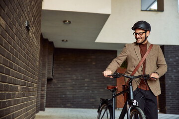 A smiling businessman with glasses on, walking on foot with a bicycle.