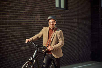Portrait of a happy businessman with a helmet and glasses on, pushing a bike.