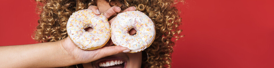 Portrait of young curly woman holding donuts on her eyes