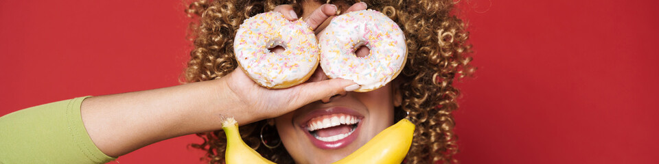 Young black woman making fun with orange and donuts