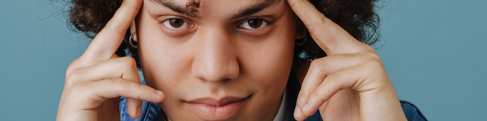 Curly young man rubbing his temples and looking at camera