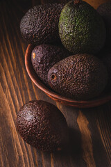 Avocado in a clay plate against a dark and moody wooden backdrop.