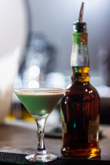 Summer alcohol drink. Tiramisu cocktail in a glass on a tall stem next to a bottle of the best rum. With copy space and bar background.