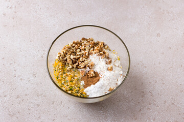 Glass bowl with mixed crushed pumpkin, eggs, sugar, oatmeal and flour, nuts and cinnamon on a beige textured background. Cooking delicious homemade autumn pastries