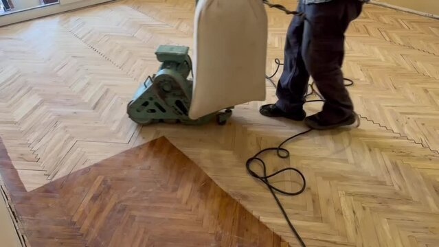 A worker is applying a scraper polish to a parquet that has deteriorated.