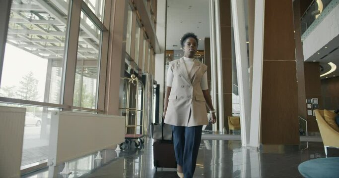 Dolly shot of serious Afro-American entrepreneur walking along hotel corridor with suitcase during business trip. People and commuting concept.