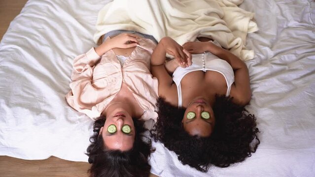 From above of diverse women lying on blanket with cucumber slices on eyes