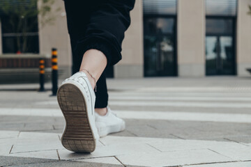 Fototapeta premium Legs of a girl in White Leather Sneakers Crosses the Street on a Pedestrian Crossing