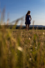 Portrait of young caucasian woman in blue dress with white hat standing on meadow