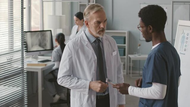 Medium shot of two diverse male medical colleagues shaking hands at workplaceMedium shot of two diverse male medical colleagues shaking hands at workplace
