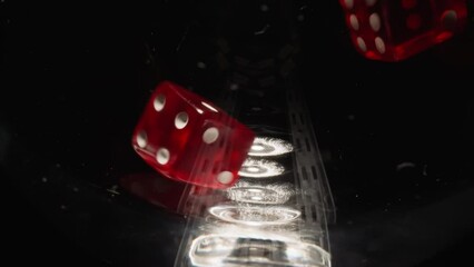 Red dices with white dots thrown into empty glass hitting on sides at bright light. Small cubes for gambling games rotate in wineglass on black background macro - Powered by Adobe