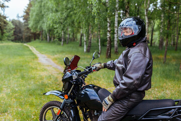 Fototapeta premium Senior motorcyclist riding motobike outdoors. Man in leather jacket resting after ride in summer forest. Space