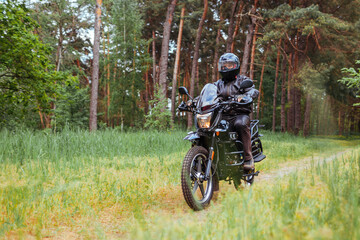 Fototapeta na wymiar Senior motorcyclist riding motobike outdoors. Man in leather jacket and helmet during ride in summer forest. Space