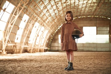Little girl in jockey clothes is standing indoors