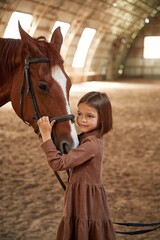 Embracing the animal. Cute little girl is with horse indoors