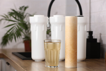 Water filter cartridge used and a glass of rusty water brown coloring on wooden table at kitchen interior. Plastic set with three filter cartridges reverse osmosis water purification system.