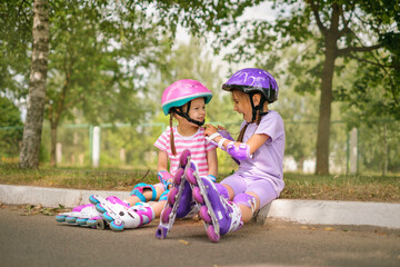 A girl helps her younger sister fasten a protective sports helmet for roller skating together in...