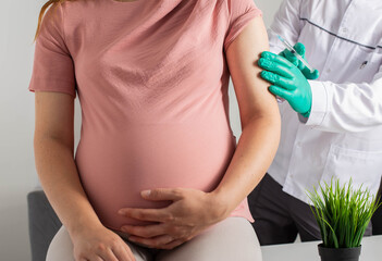 A doctor in medical gloves vaccinates a pregnant girl against flu, covid and whooping cough.